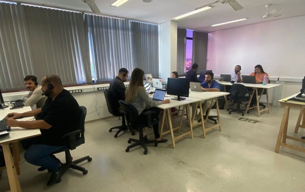 Empresa de Outbound: Um grupo de pessoas trabalhando em um ambiente de escritório, com mesas, computadores e cadeiras de escritório visíveis. A sala possui um layout moderno e aberto, com grandes janelas e luminárias.