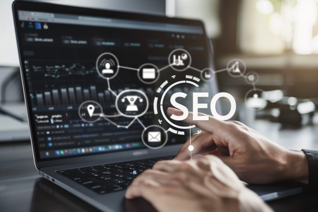 SEO para empresas: As mãos de uma pessoa digitando em um teclado de laptop, com um ícone de otimização de mecanismo de busca (SEO) e ícones relacionados exibidos na tela do laptop.
